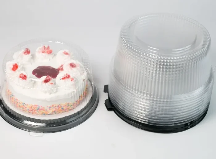 "Round clear cake container by JC Packaging showcasing a frosted cake with colorful sprinkles and strawberry toppings, with an additional stack of clear containers on the right."