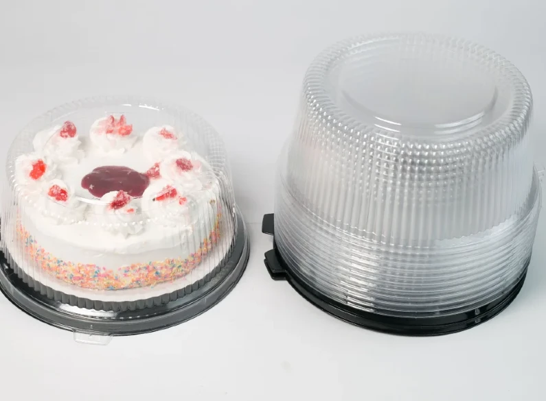 "Round clear cake container by JC Packaging showcasing a frosted cake with colorful sprinkles and strawberry toppings, with an additional stack of clear containers on the right."