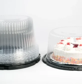 "A frosted cake with colorful sprinkles and strawberry topping in a JC Packaging clear cake container, beside an empty stack of clear containers, all against a clean white background."