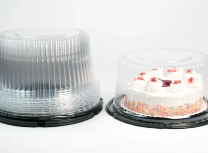 "JC Packaging's large clear cake dome secures a delectable frosted cake with strawberry toppings, adjacent to a similar empty dome, showcasing clarity and space."