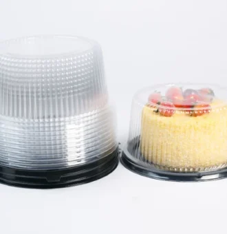 "Premium clear cake containers by JC Packaging, with a golden sponge cake adorned with fresh strawberries under the dome, next to a stack of clear domes on a white background."