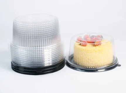 "Premium clear cake containers by JC Packaging, with a golden sponge cake adorned with fresh strawberries under the dome, next to a stack of clear domes on a white background."