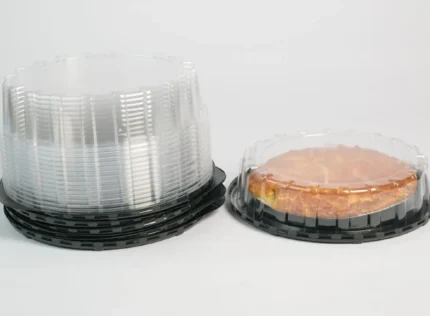 "Stack of JC Packaging's clear containers for cakes and tarts on black bases, featuring a delicious tart in a transparent package, ready for display."