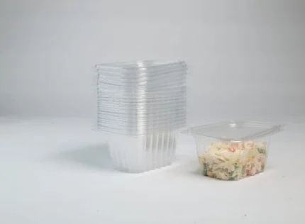 "A stack of transparent large salad containers next to a filled one showcasing a mixed salad, emphasizing the spacious and clear design by JC Packaging."