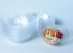 "A stack of Burger Dome containers next to a filled Burger Dome, highlighting the product's clarity and design by JC Packaging."