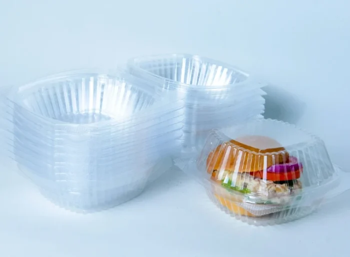 "A stack of Burger Dome containers next to a filled Burger Dome, highlighting the product's clarity and design by JC Packaging."