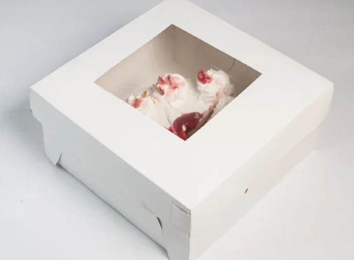 "Delectable strawberry cake partially visible through the window of a chic white paper cake box - order yours at www.jcpackaging.net"