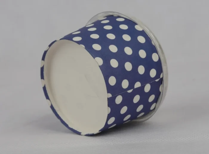 "A medium-sized ice cream cup adorned with white polka dots on a navy blue background, featuring a transparent dome lid, from www.jcpackaging.net."