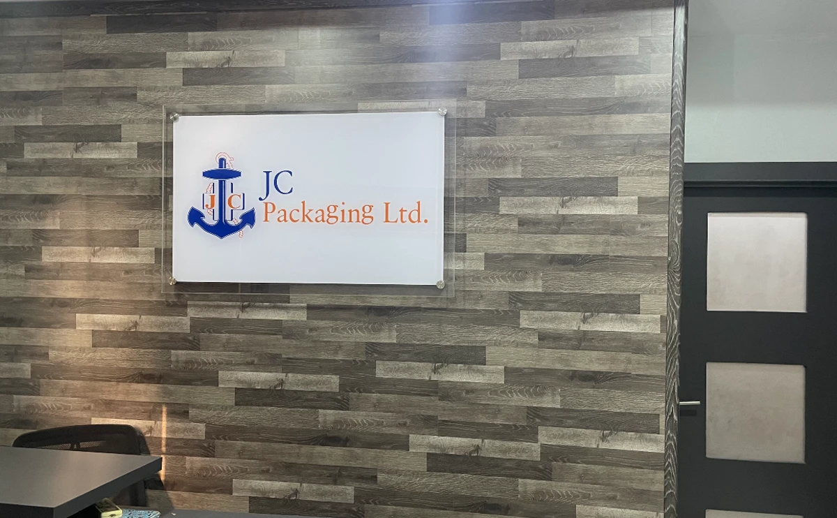 "The 'About Us' wall of JC Packaging Ltd featuring their logo on a stylish wooden backdrop within their office, symbolizing the company's commitment to quality and detail, visit www.jcpackaging.net to know more."