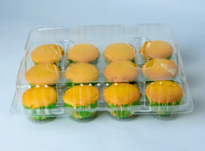 "Clear packaging displaying a dozen golden-baked muffins by JC Packaging, perfect for showcasing bakery products."