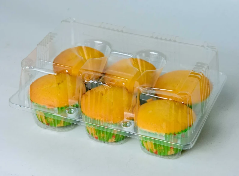 "Transparent six-muffin display case by JC Packaging featuring golden yellow muffins with green and orange paper liners, highlighting product clarity and baked good appeal."