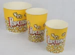 "Three yellow popcorn buckets with 'Popcorn' text and popping kernels design by www.jcpackaging.net, showcasing different sizes."