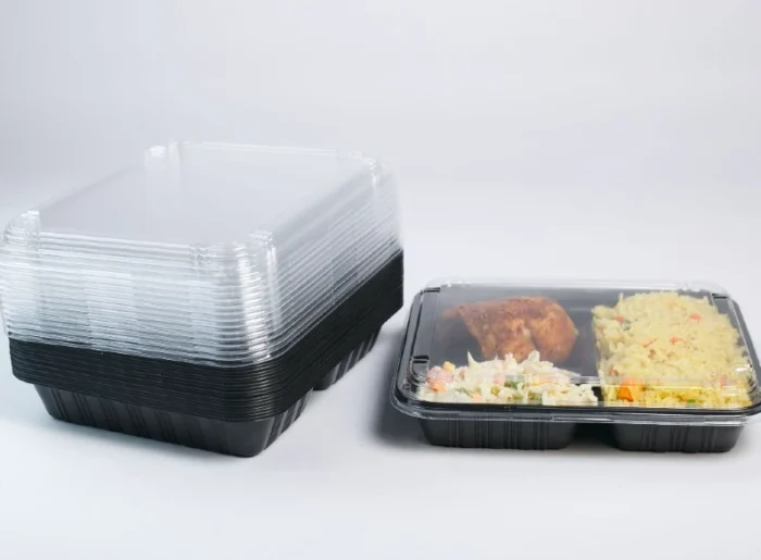"Stack of premium black Meal Prep Tray Packaging next to a ready meal, showcasing the perfect blend of convenience and quality at www.jcpackaging.net"