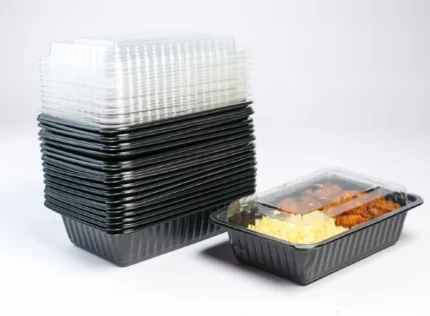 "A stack of JC Packaging's single compartment meal boxes with transparent lids alongside an open container filled with a delicious meal, exemplifying ideal food packaging solutions."