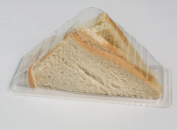 "Stacks of JC Packaging's clear sandwich wedge containers alongside a filled example, emphasizing quantity and quality - more at jcpackaging.net."